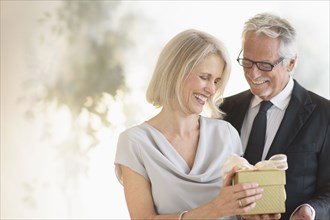 Smiling older Caucasian man giving wife a gift