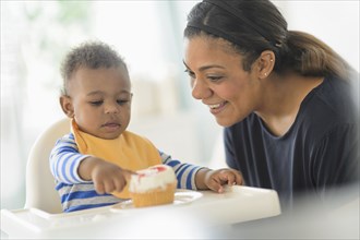 Mixed race mother giving baby son cupcake in high chair