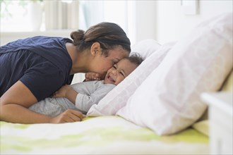 Mixed race mother kissing baby son on bed