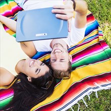 Hispanic couple taking selfie on blanket in park