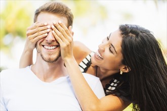 Hispanic woman covering eyes of boyfriend outdoors