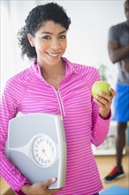 Woman holding apple and scale in gym
