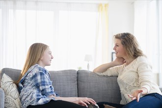 Caucasian mother and daughter talking on sofa