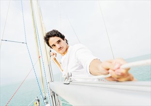 Hispanic man adjusting rigging on sailboat