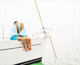 Couple wrapped in towels on deck of sailboat