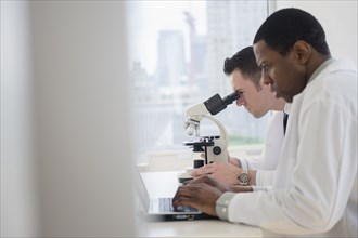 Scientists using laptop and microscope in lab