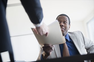 Businessman handing folder to boss in office