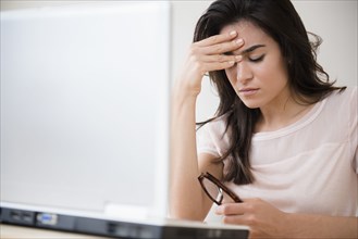Stressed woman rubbing her forehead at laptop