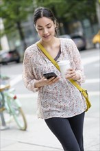 Hispanic woman using cell phone on city sidewalk