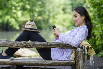Hispanic woman using cell phone on park bench