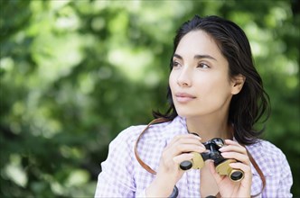 Hispanic woman using binoculars outdoors