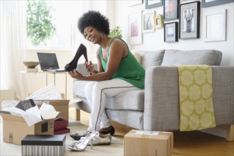 African American woman opening packages of shoes on sofa