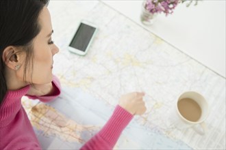 Mixed race woman reading roadmap with coffee