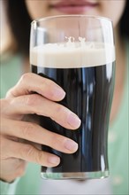 Mixed race woman drinking glass of dark beer