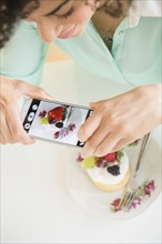 Mixed race woman taking cell phone photograph of dessert