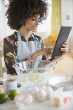 Mixed race woman baking with recipe on digital tablet