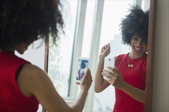 Mixed race woman taking selfie with cell phone in mirror