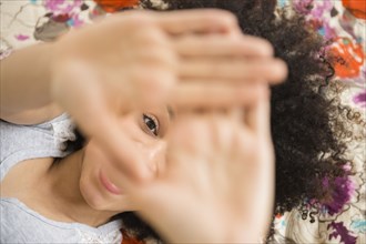 Mixed race woman peering through fingers on bed