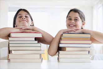 Caucasian twin sisters resting on stacks of books