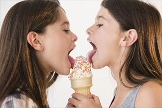 Caucasian twin sisters sharing ice cream cone