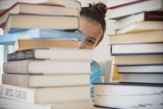 Girl peeking from behind stacks of books