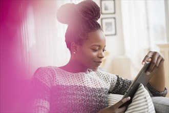 Black woman using digital tablet on sofa