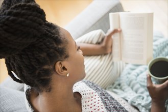 Black woman reading book and drinking coffee