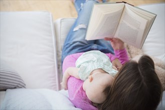 Mother reading book and holding baby daughter