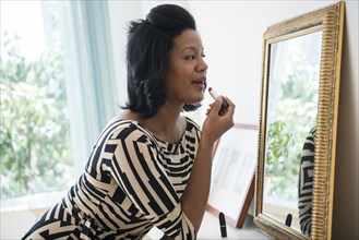 Black woman applying lipstick in mirror