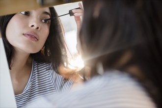 Hispanic woman applying mascara in mirror