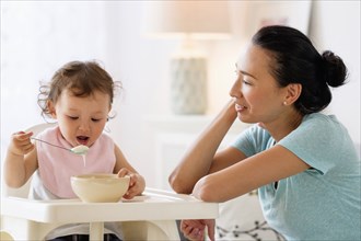 Mother watching baby daughter eat in high chair