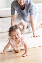 Mother and baby daughter crawling in living room