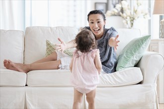 Mother reaching for baby daughter on sofa