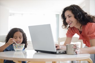 Mother using laptop at breakfast with daughter