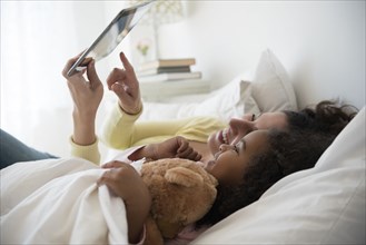 Mother and daughter using digital tablet in bed