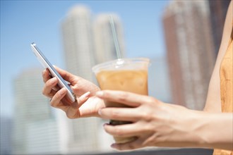 Hispanic woman holding cell phone and iced coffee