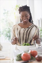Black woman tossing salad in kitchen