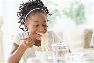 Black girl eating noodles at table
