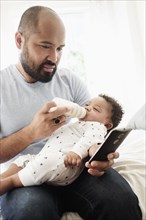 Father bottle feeding baby son and using cell phone