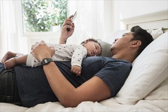 Father using cell phone with sleeping baby son