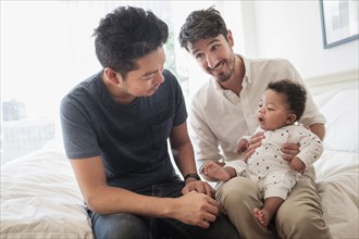 Gay fathers playing with baby son on bed