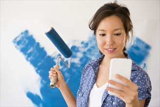 Mixed race woman using cell phone and painting wall
