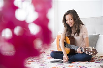 Mixed race woman playing guitar on bed
