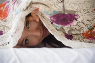 Mixed race woman peeking out from blanket