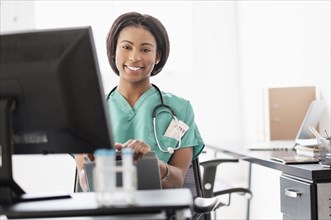 Mixed race nurse smiling at computer