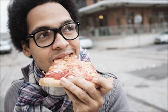 Mixed race man eating pizza outdoors