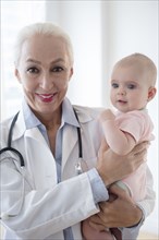 Caucasian pediatrician holding baby patient