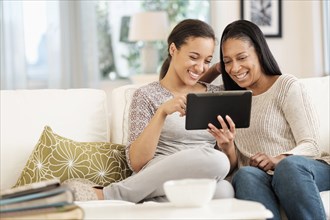 Mother and daughter using digital tablet on sofa