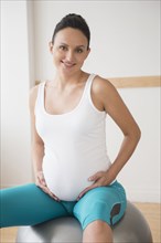 Pregnant Caucasian woman on fitness ball holding belly