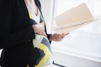 Pregnant Caucasian businesswoman holding files in office